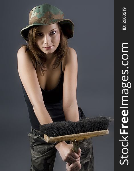 Attractive brunette military girl with a camouflage hat and black shirt holding broom. Attractive brunette military girl with a camouflage hat and black shirt holding broom