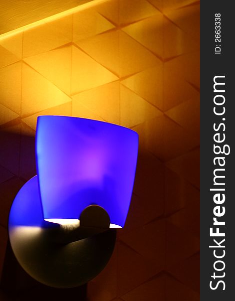 A modern blue light fixture against a gold wall. A modern blue light fixture against a gold wall