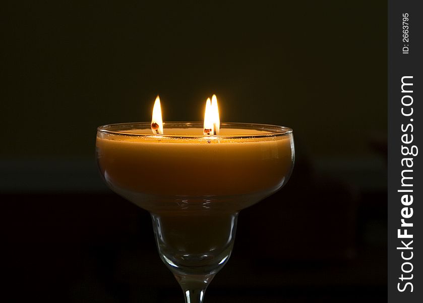 Orange candle with three flames in a pitch dark room