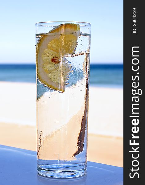 Fresh glass of bubble water with a slice of lemon at the beach