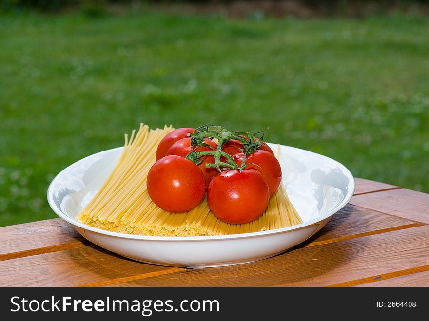 plate with spaghetti and tomato on table in garden. plate with spaghetti and tomato on table in garden