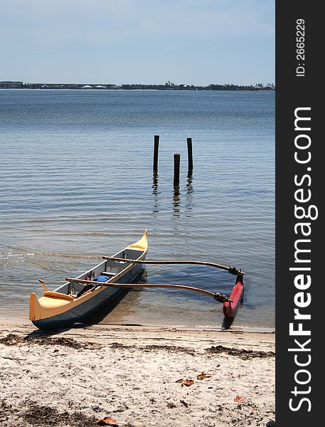 Colorful outrigger canoe beached at the shore.
Vertical orientation.  Blue sky, calm waters.