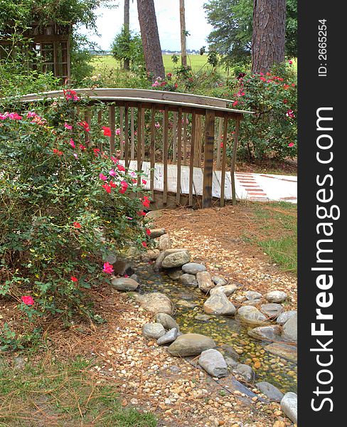 Wooden ornate foot bridge along garden path through a rose garden. vertical orientation. Wooden ornate foot bridge along garden path through a rose garden. vertical orientation.