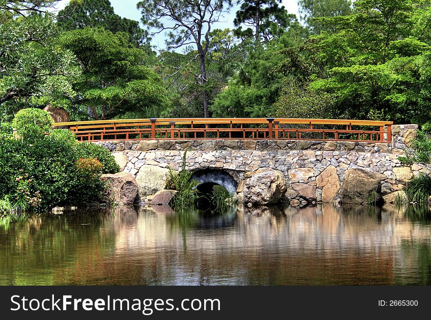 Stone bridge over lake in a pristine garden environment. Reflection of bridge in water.