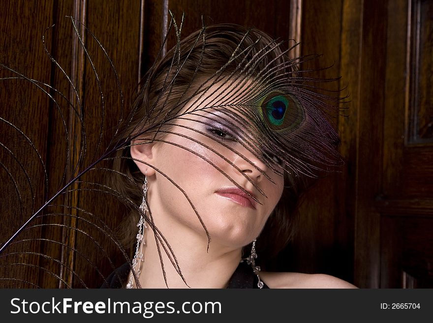 Beautiful young brunette woman with a feather partially covering her face. Dark wood background. Beautiful young brunette woman with a feather partially covering her face. Dark wood background.