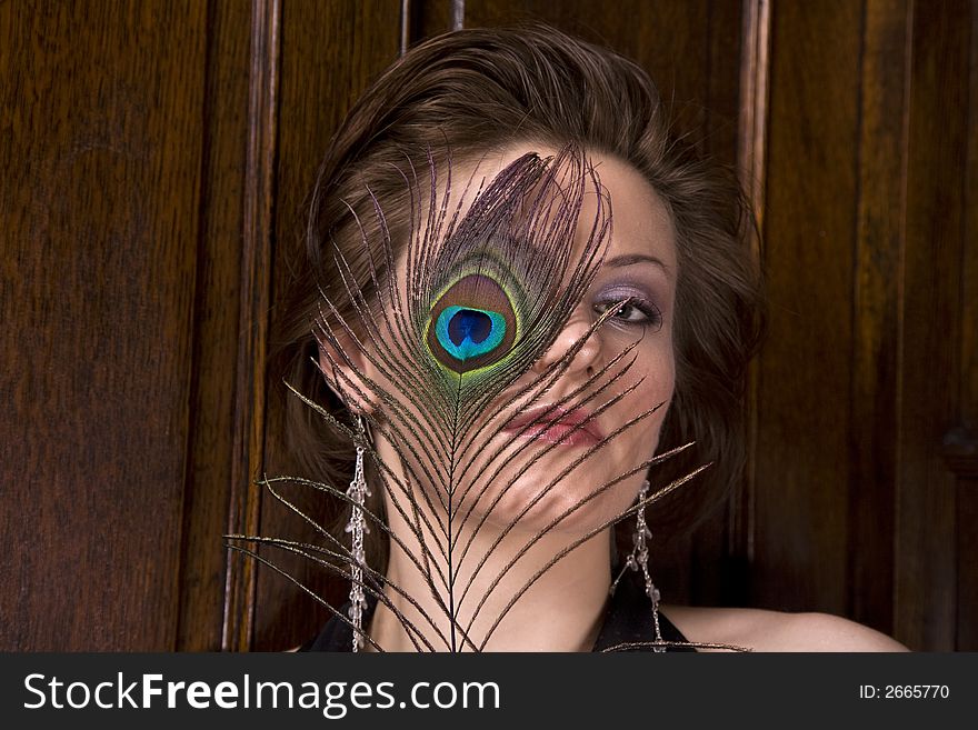 Beautiful young brunette woman with a feather partially covering her face. Dark wood background. Beautiful young brunette woman with a feather partially covering her face. Dark wood background.
