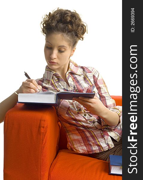 Young, beautiful woman sitting on orange couch. Writing on book. White background. Young, beautiful woman sitting on orange couch. Writing on book. White background