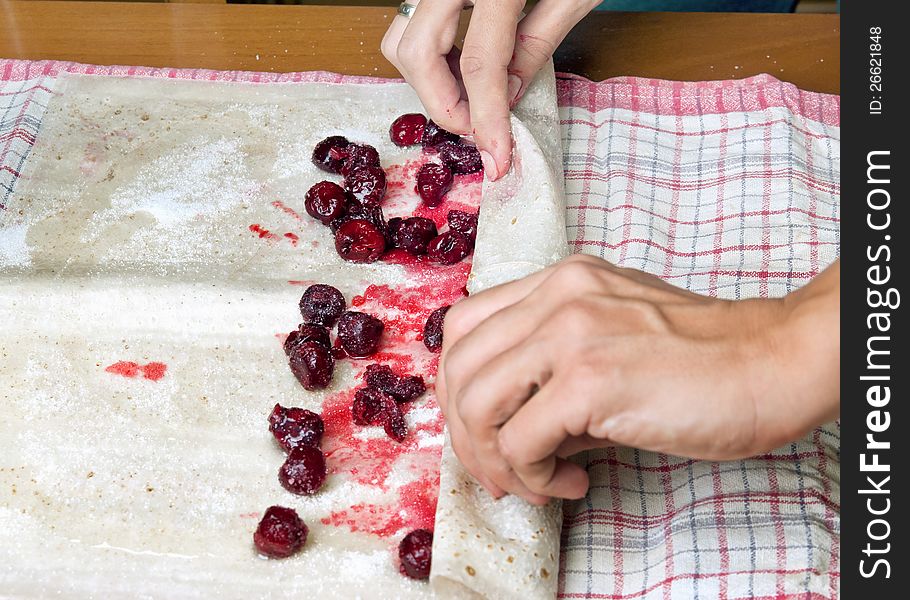 Female hands making small pies with cherry on a table