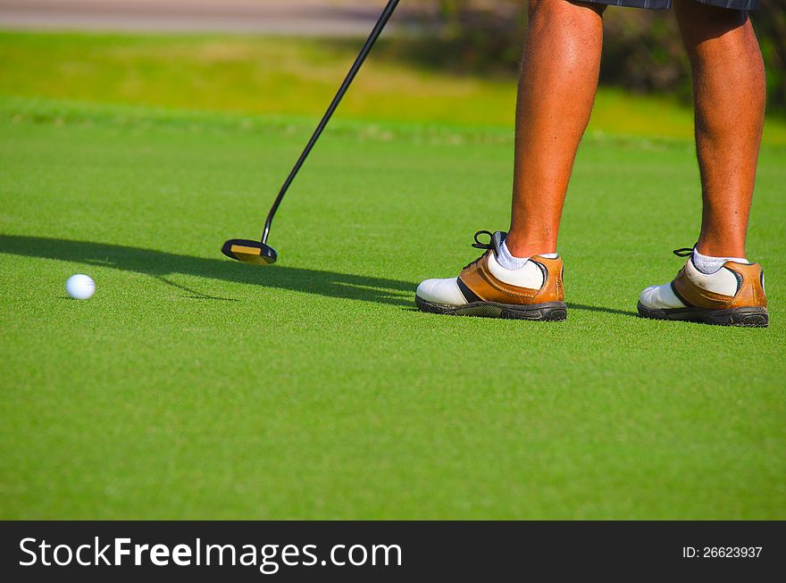 Closeup of golfer putting on the green with the ball in motion and the golfer finishing his swing. Closeup of golfer putting on the green with the ball in motion and the golfer finishing his swing.