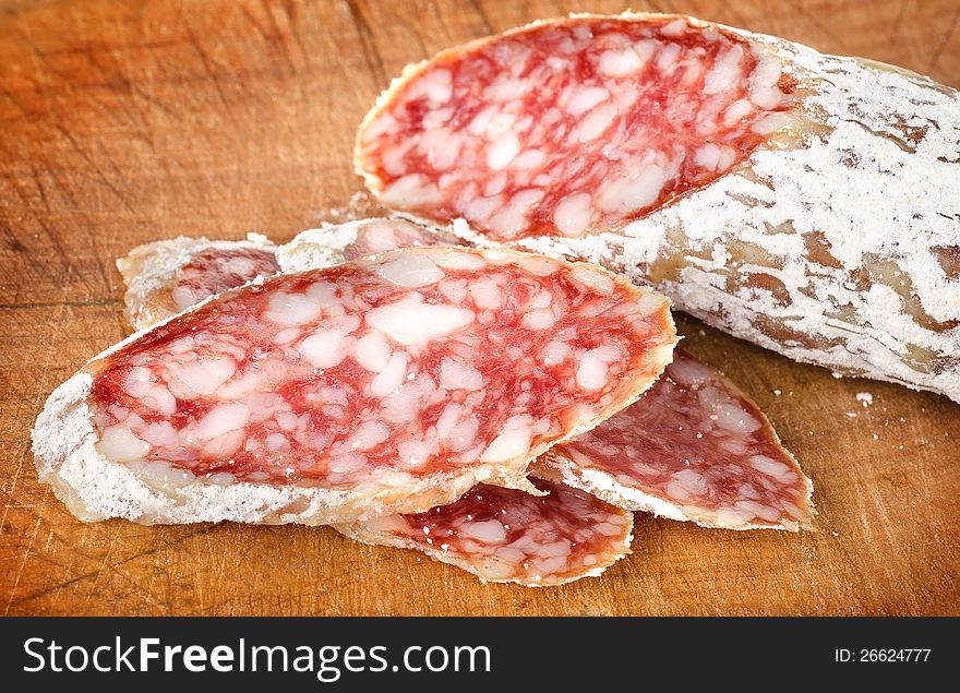 Ð¡hopping a salami on a dark wooden cutting board. Ð¡hopping a salami on a dark wooden cutting board