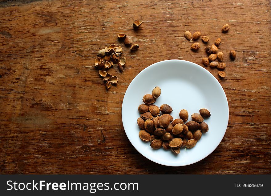 Small white plate of apricot seeds on a rustic table