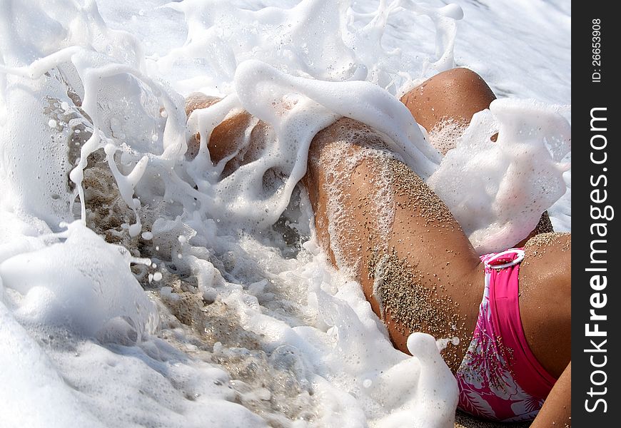 Sandy legs of woman lying in sea with breaking surf . Sandy legs of woman lying in sea with breaking surf .