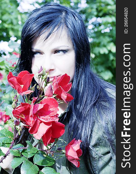 Beautiful brunette near red roses with buds in dew drops