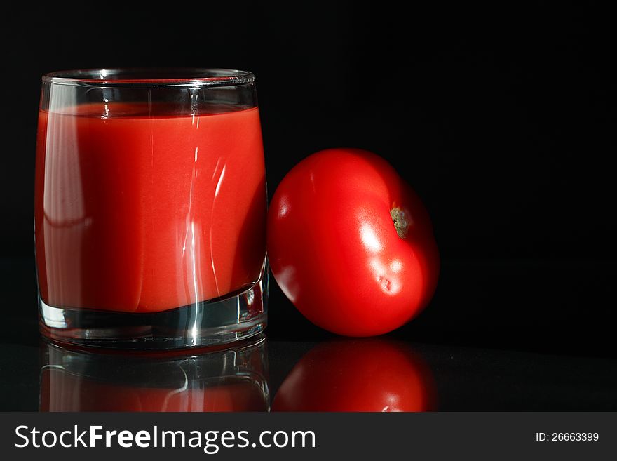 Glass of tomato juice near tomato on black background