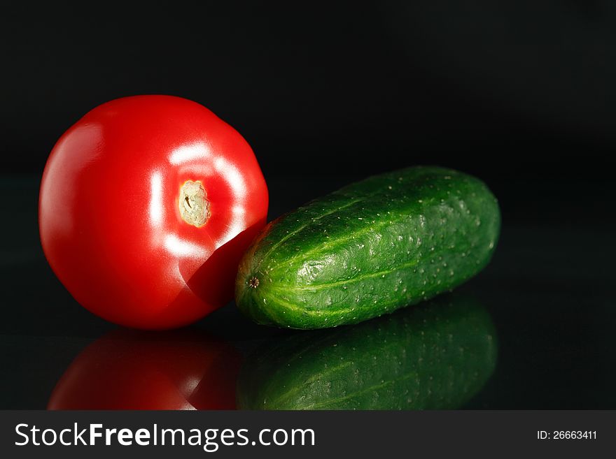 Freshness red tomato and green cucumber on black background with reflection. Freshness red tomato and green cucumber on black background with reflection