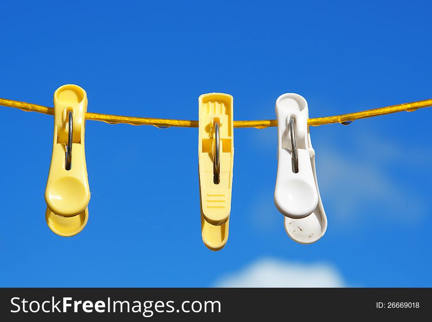 Three clothespins on a yellow cord on a background of blue sky