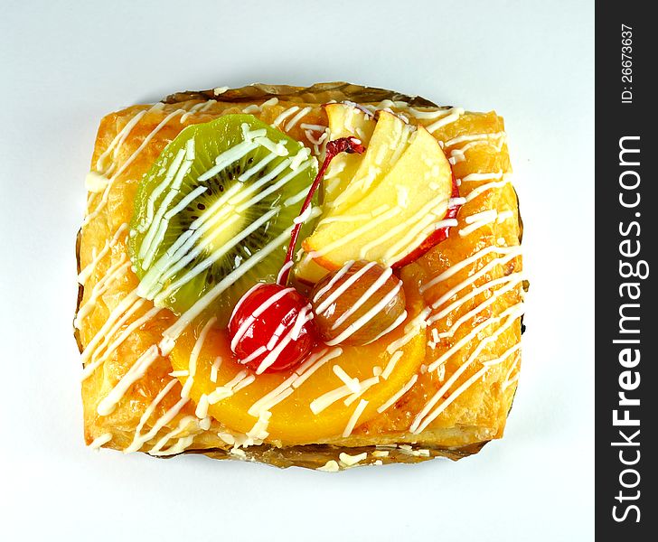 Freshly baked sweet fruit danish on white plate with many fruit such as cherry, grape, peach, kiwi and apples on top