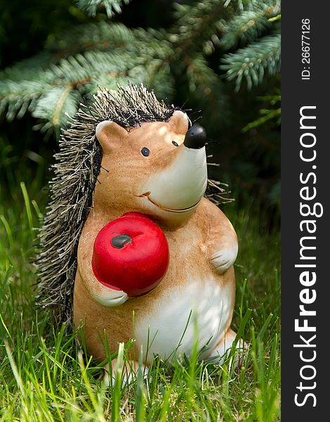 Clay hedgehog standing in the garden on the grass and holding a red apple. Clay hedgehog standing in the garden on the grass and holding a red apple