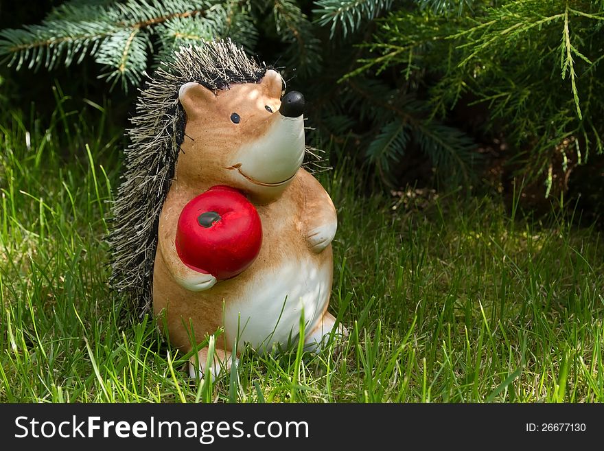 Clay hedgehog standing in the garden on the grass and holding a red apple. Clay hedgehog standing in the garden on the grass and holding a red apple