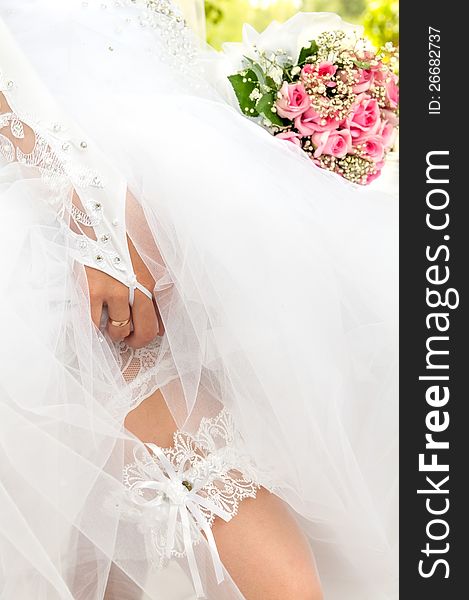 The bride with a bouquet of lifting up the bottom of her dress shows the garter on the mattress. The bride with a bouquet of lifting up the bottom of her dress shows the garter on the mattress