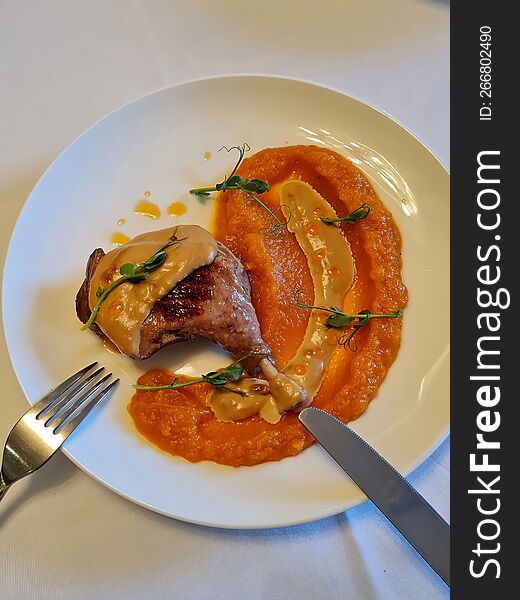 Chicken leg with pumpkin sauce on a white round plate