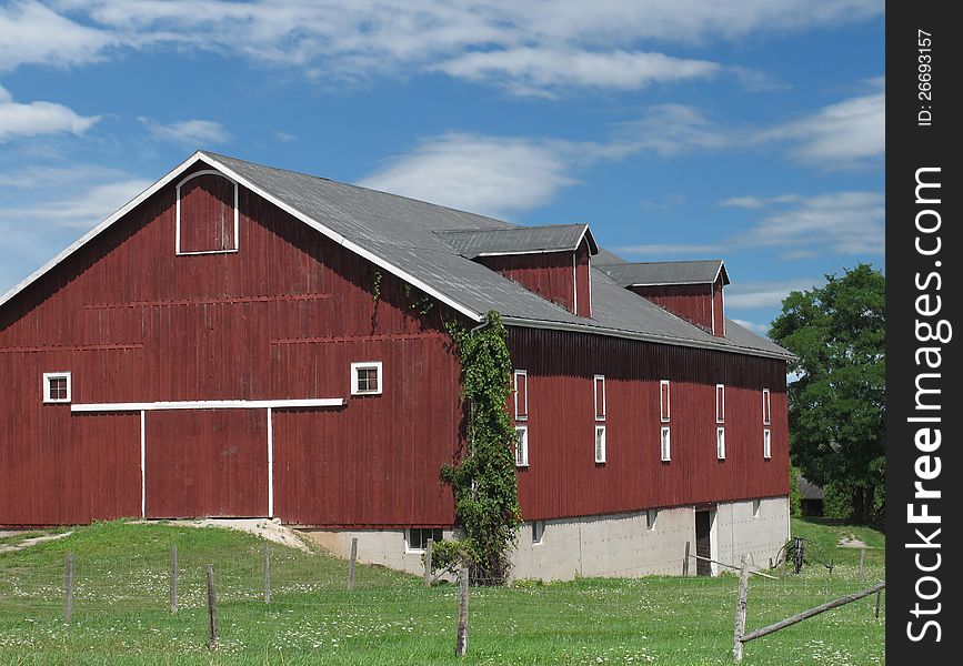 Large red wooden farm barn and barnyard, with blue sky and clouds. Large red wooden farm barn and barnyard, with blue sky and clouds.
