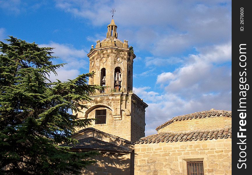 Church bell tower next to tall tree with cloudy blue sky backdrop. Church bell tower next to tall tree with cloudy blue sky backdrop