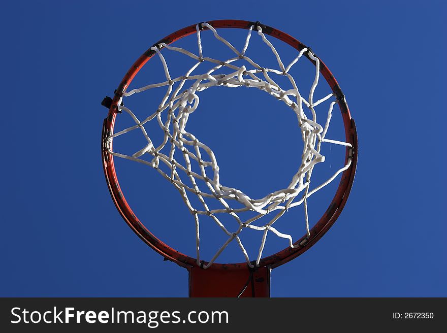 Basketball hoop as viewed from below against a bright blue sky.