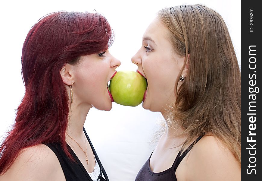 Two girls bite a green apple. Two girls bite a green apple