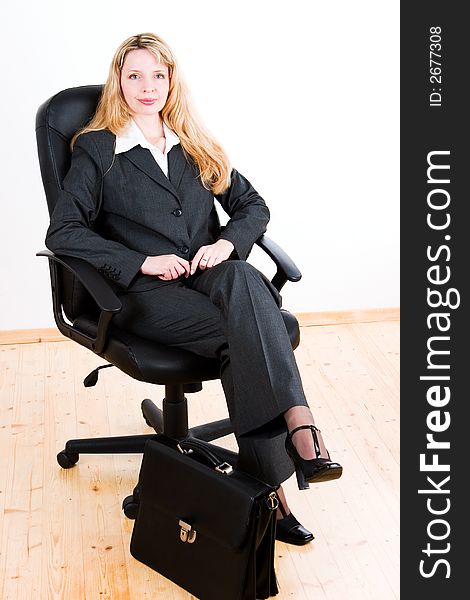 A business woman sitting in a big black chair with a case at her feet. A business woman sitting in a big black chair with a case at her feet