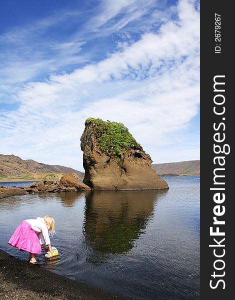 A cute little blond girl playing at the waters edge with grown cliffs and blue sky in background. A cute little blond girl playing at the waters edge with grown cliffs and blue sky in background