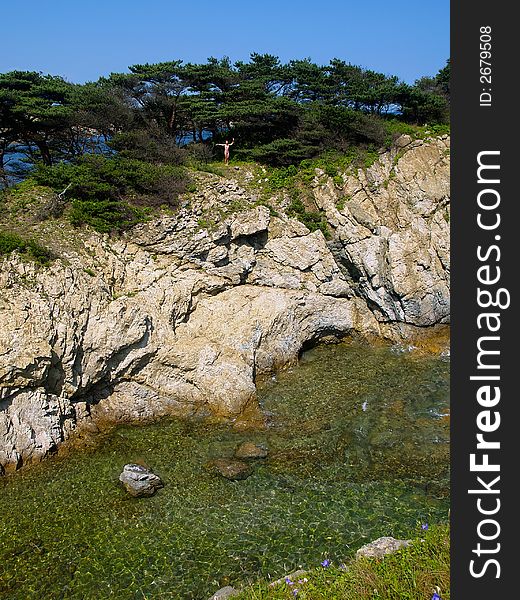 sea landscape showing young girl standing on the seaside rock with pines