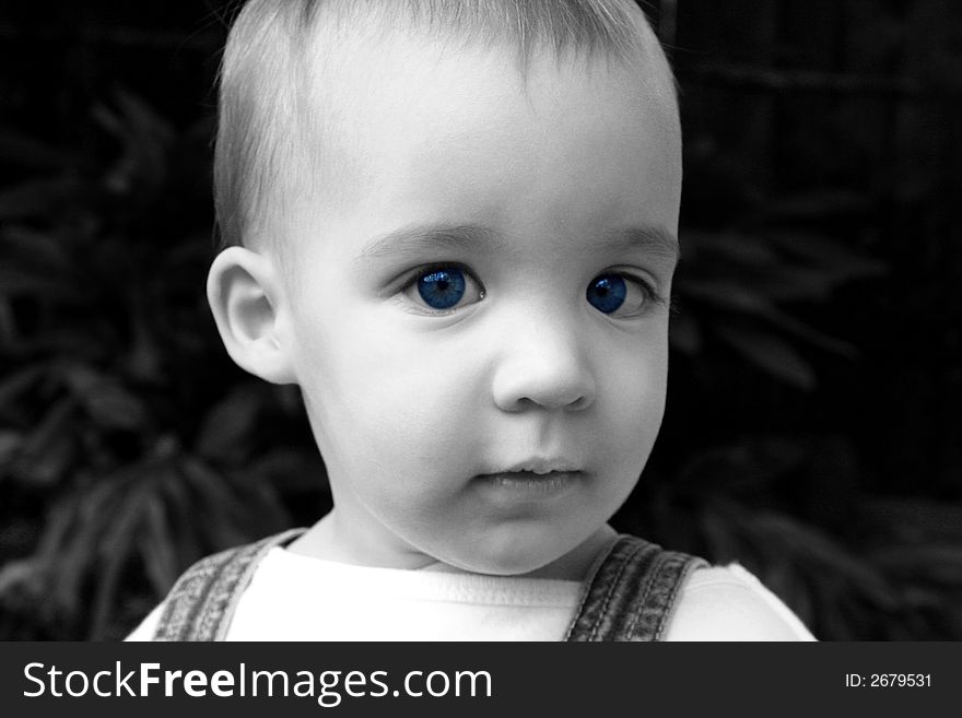 This is a close-up of a young child with vibrant blue eyes in which the eyes are in color and the rest of the photo is in black and white.