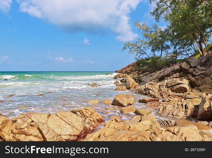 Seascape. The waves of the sea, rocks, trees on the hill and clouds in the sky.