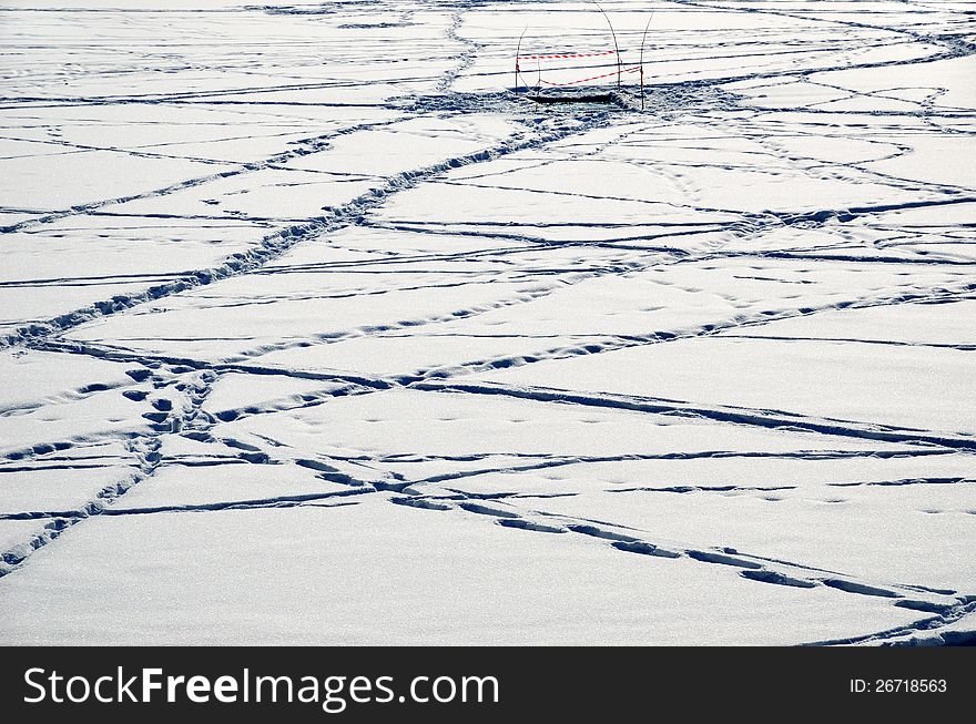 Fenced ice-hole is in the middle of the snow cover of the pond with many footprints. Fenced ice-hole is in the middle of the snow cover of the pond with many footprints.