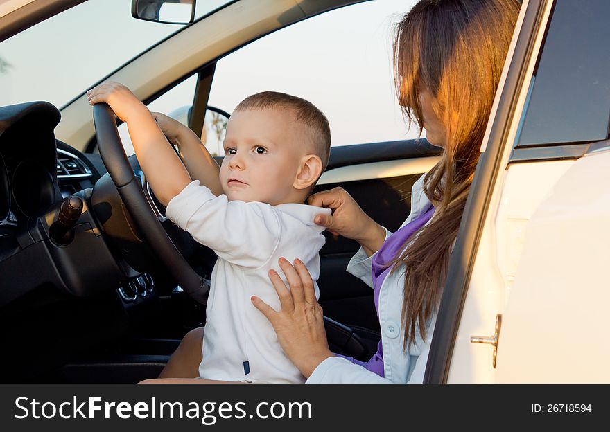 Small boy pretending to drive with his hands on the steering wheel while seated on his mothers lap