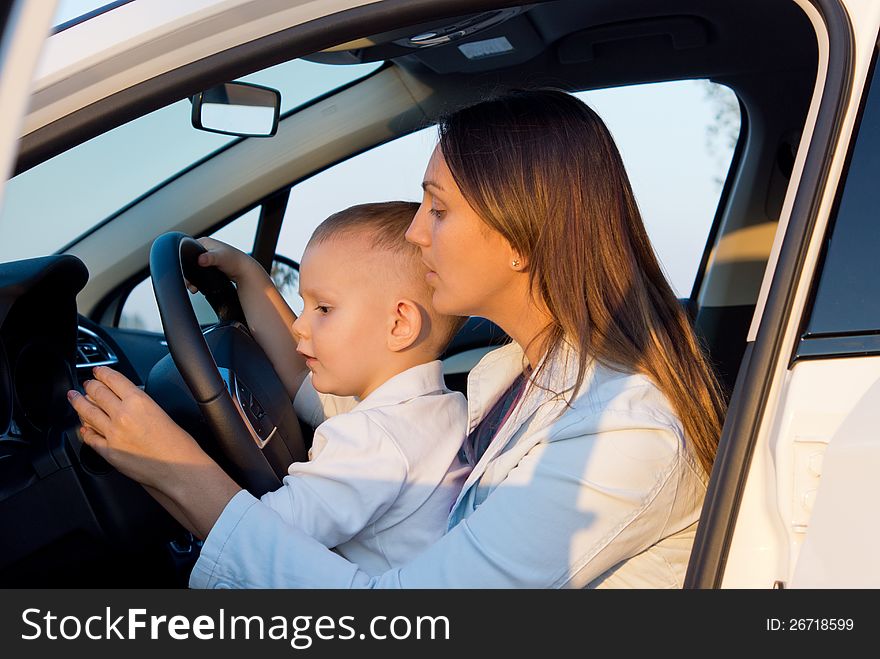 A young mother teaching her small son who is sitting on her lap to drive by showing him the indicators. A young mother teaching her small son who is sitting on her lap to drive by showing him the indicators