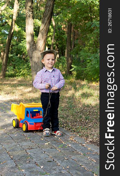 Cute little boy pulling a colourful toy truck behind him on a paved lane in woodland. Cute little boy pulling a colourful toy truck behind him on a paved lane in woodland