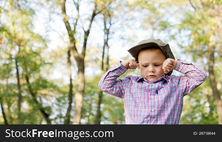 Low angle view of an upset frowning little boy with his hands balled into fists on either side of his forehead outside in woodland with copyspace. Low angle view of an upset frowning little boy with his hands balled into fists on either side of his forehead outside in woodland with copyspace.