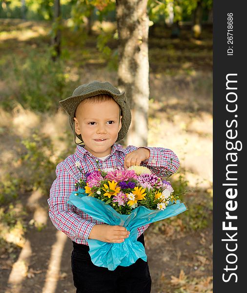 Mischievous little boy in a cowboy style hat holding a large bouquet of giftwrapped flowers standing in woodland. Mischievous little boy in a cowboy style hat holding a large bouquet of giftwrapped flowers standing in woodland