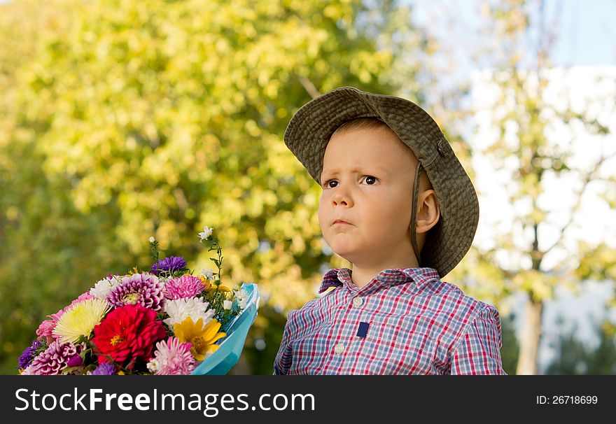 Concerned little boy with a large bunch of colourful flowers waiting to give them to his mother on Mothers Day or Valentines with copyspace. Concerned little boy with a large bunch of colourful flowers waiting to give them to his mother on Mothers Day or Valentines with copyspace