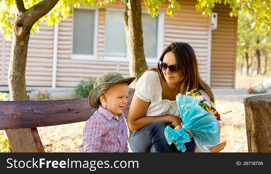 Little boy giving Mum a bouquet of flowers on Mothers Day or Valentines to show his love for her on a rustic bench near a cabin