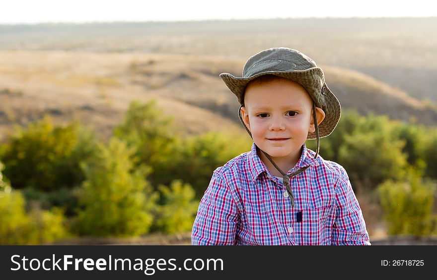 Young boy in a cute sunhat posing in front of a lovely view of open countryside with copyspace. Young boy in a cute sunhat posing in front of a lovely view of open countryside with copyspace