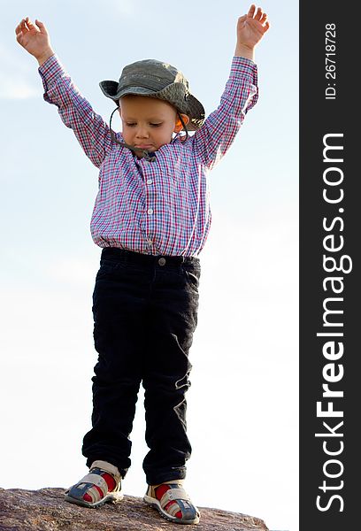 Little boy having fun standing with his arms raised balanced on the top of a rock. Little boy having fun standing with his arms raised balanced on the top of a rock