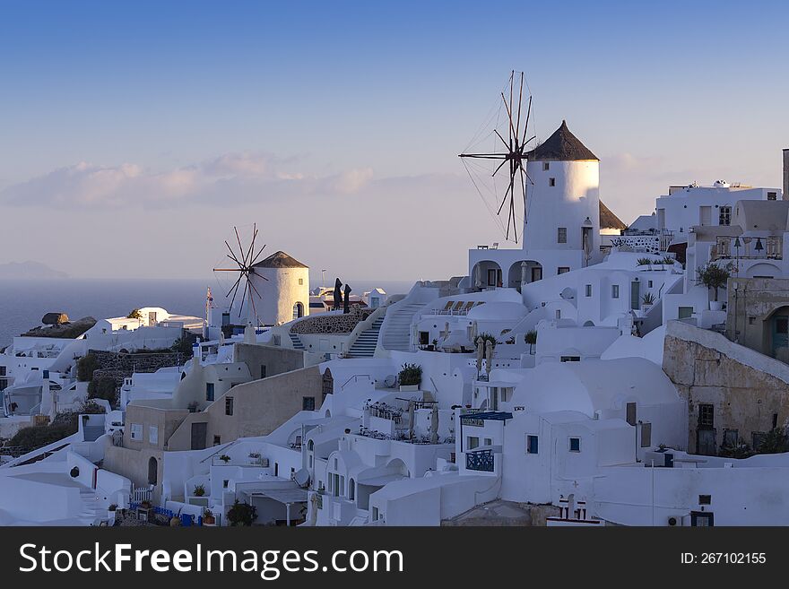 Santorini - Oia, view of white windmills on the slopes of the island. Around are white, picturesque houses between the stone streets. Beautiful sky