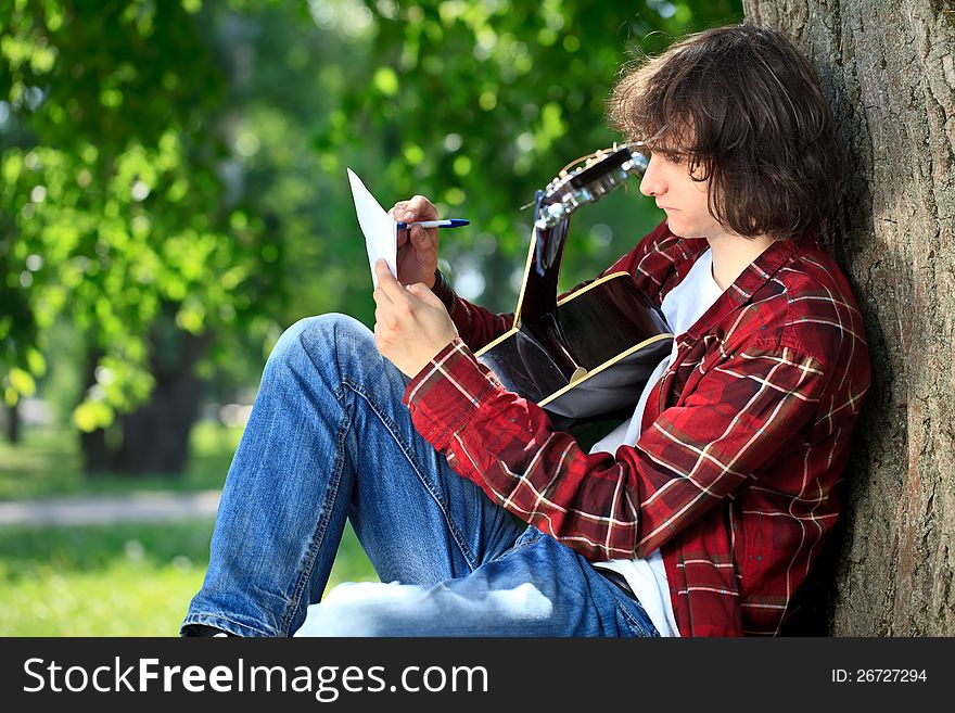 Man composing song on guitar in park