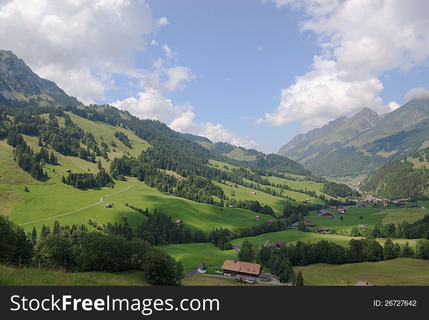 Summer rural landscape view on green Alps mountains, trees, slopes, and detached wooden houses in valley. Alps, Switzerland, europe. Summer rural landscape view on green Alps mountains, trees, slopes, and detached wooden houses in valley. Alps, Switzerland, europe.