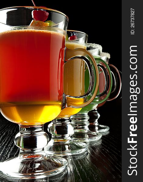 Group of four wine glasses with colored alcoholic cocktails, decorated with fruit and sugar on black bar counter