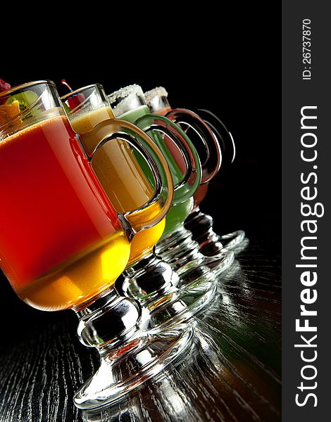 Group of four wine glasses with colored alcoholic cocktails, decorated with fruit and sugar on black bar counter