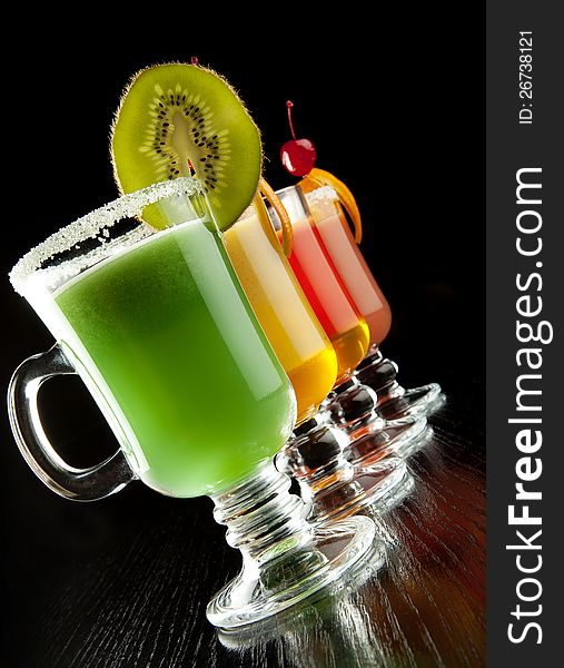 Group of four wine glasses with colored alcoholic cocktails, decorated with fruit and sugar on black bar counter